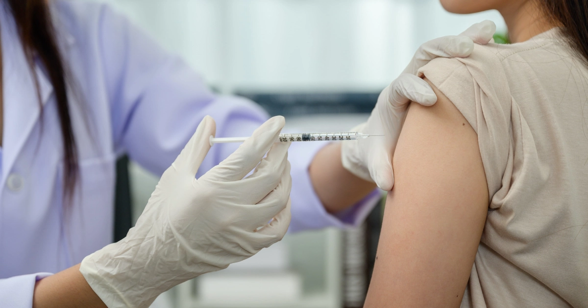 A healthcare professional in white gloves administering an injection with a syringe into the upper arm of a patient for Flu Shots and Vaccinations in Braselton, Cumming, and Duluth.